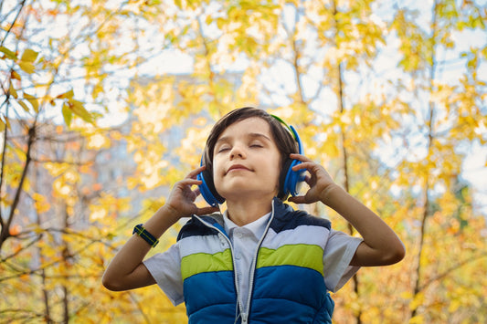 Garçon les yeux fermés écoutant au casque d'écoute devant des arbres aux feuilles jaunes