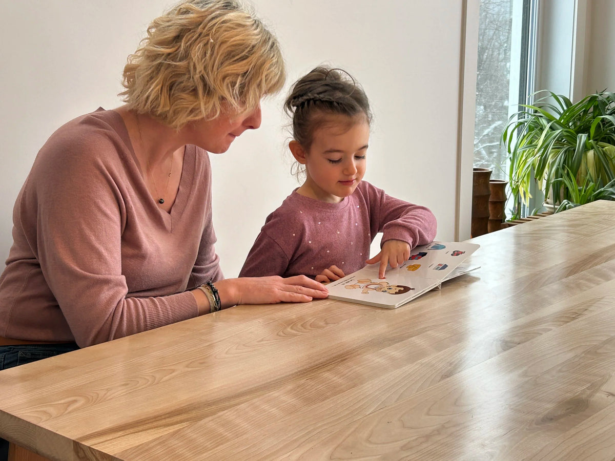 Éducatrice et fillette regardant ensemble un livre Symbolicone à une table en bois