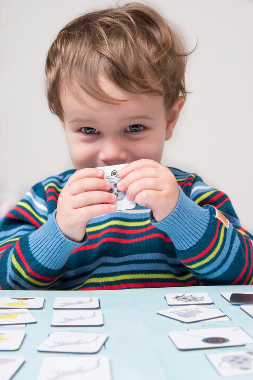 Jeune enfant tenant une carte de pictogramme à deux mains, d'autres cartes étalées sur la table