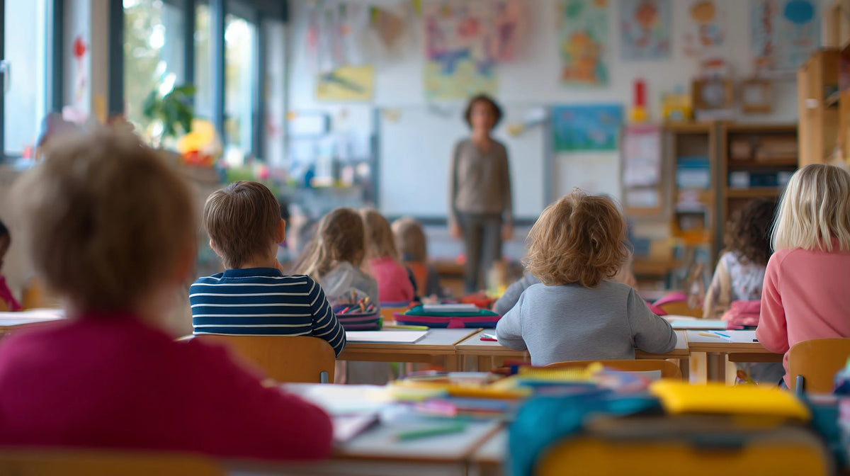 Salle de classe colorée où des enfants assis écoutent leur enseignante debout